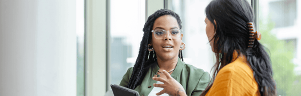 Two women talking at work, by a window
